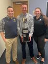 Two male and one female Athletic Training students shown in classroom, holding Quiz Bowl trophy.