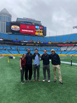 Sport management students and faculty member stand together on field at Dukes Mayo Bowl game