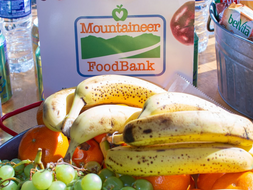 Bananas, grapes and oranges sit outside in front of a Mountaineer Foodbank sign