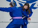 A student wearing a blue gi practices jiu-jitsu moves on another student.
