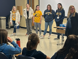 WVU students and professor stand and present in front of a group of elementary students.