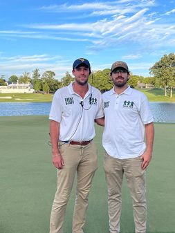 Andrew Walker, on left, with Justin Violette, standing on a golf course, wearing event white shirts and tan pants. 