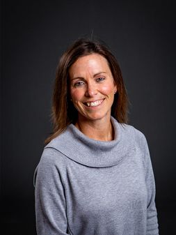 Lindsey Blom portrait photo wearing light grey sweater, with long brown hair. 