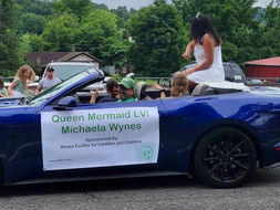 Micheala Wynes rides in the back of a blue car in a parade.