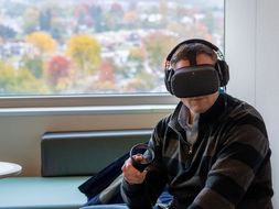 A student sits with a virtual reality headset with fall foliage in the background.