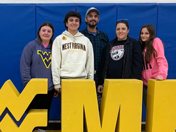 Tyler Derkotch poses with his family in front of a WVU "HOME" sign in a gymnasium.
