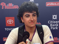 Tyler Kerkotch talks into a microphone in front of a Philadelphia Phillies backdrop.