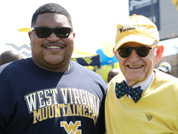 Jihad Dixon wearing WVU dark blue tshirt, standing next to President Gee, wearing a gold hat and vest and WVU bowtie.