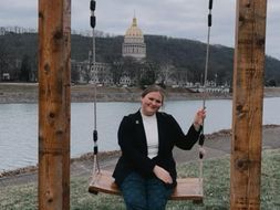 Abbey Clark sits on a swing with the West Virginia state capitol building in the background.