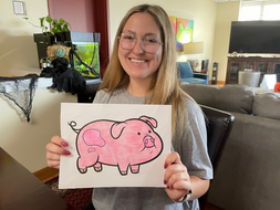 Marissa Mangione is holding a picture of a pig that she colored.
